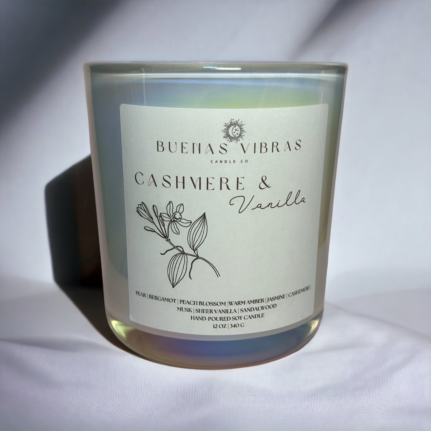 A candle in a glass jar with a label that reads "Buenas Vibras Candle Co. Cashmere & Vanilla," featuring a botanical illustration.