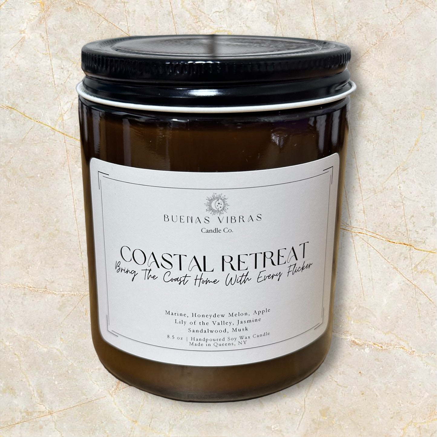 Brown candle jar with a label reading "Coastal Retreat" by Buenas Vibras Candle Co., featuring marine, honeydew melon, apple, lily of the valley, jasmine, and sandalwood scents.